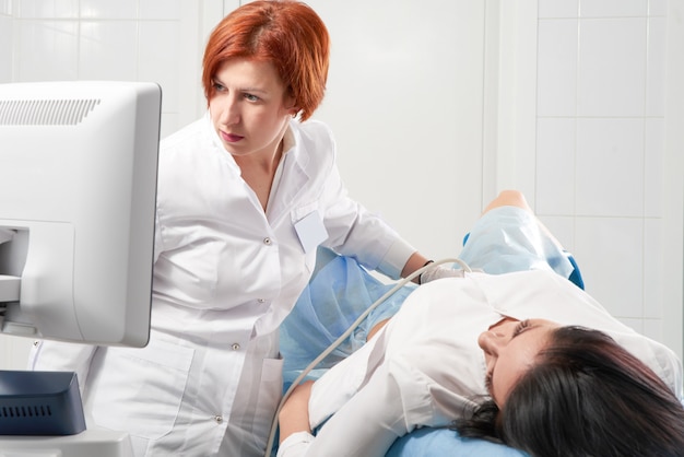 Ginecologo tenendo la bacchetta ad ultrasuoni transvaginale dopo aver esaminato una donna e mostrando i risultati su uno schermo