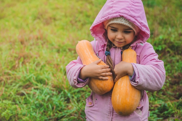 Giocando all'aperto ragazza carina che tiene una zucca. Raccolta delle zucche, autunno in giardino, la bella ragazza e grandi zucche.