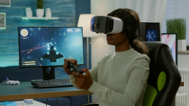 Giocatore africano che gioca a una competizione di sparatutto spaziale utilizzando occhiali per realtà virtuale. Giocatore competitivo che utilizza il joystick per il campionato online seduto su una sedia da gioco a tarda notte in soggiorno