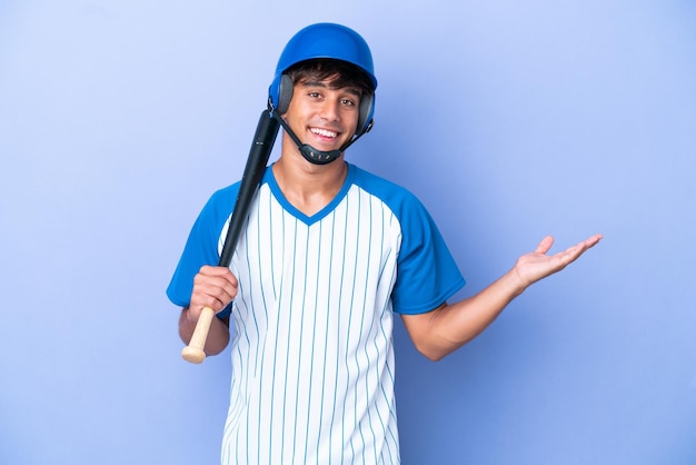 Giocatore di baseball caucasico con casco e pipistrello isolato su sfondo blu che estende le mani di lato per invitare a venire