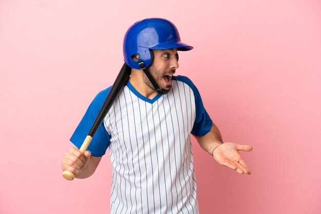 Giocatore di baseball con casco e mazza isolato su sfondo rosa con espressione di sorpresa mentre guarda di lato