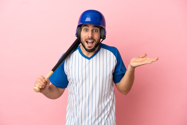 Giocatore di baseball con casco e mazza isolato su sfondo rosa con espressione facciale scioccata