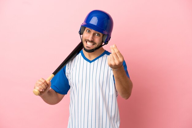 Giocatore di baseball con casco e pipistrello isolato su sfondo rosa che fa gesto di denaro