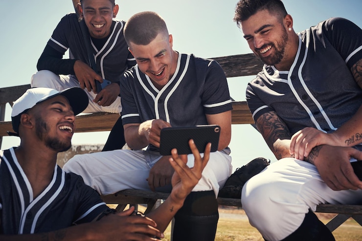 Foto giocatore di baseball uomini e felici con smartphone per la discussione di squadra con video di strategia o diversità in pausa allo stadio gruppo di persone e revisione per gioco concorso o allenamento su app mobile a los angeles