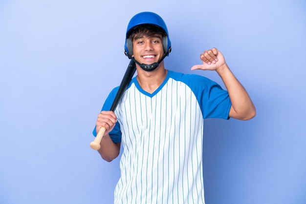 Giocatore di baseball uomo caucasico con casco e mazza isolato su sfondo blu orgoglioso e soddisfatto di sé