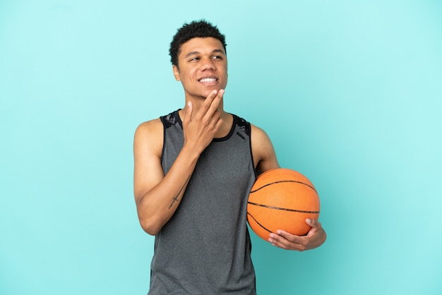 Giocatore di basket uomo afroamericano isolato su sfondo blu guardando in alto mentre sorride