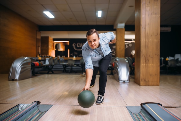 Giocatore di bocce maschio lancia la palla sulla corsia, vista frontale. Giocatore di bowling, lancio in azione, classico gioco tenpin nel club, tempo libero attivo