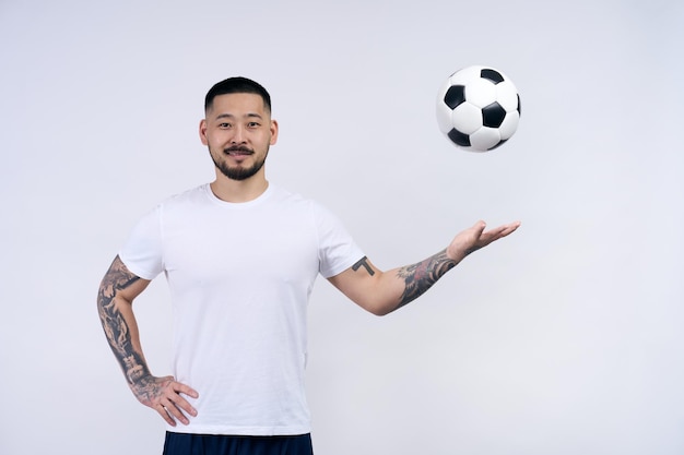 Giocatore di calcio sportivo motivato asiatico che lancia palla guardando la fotocamera