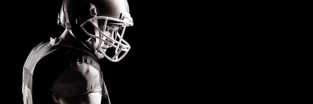 Giocatore di football americano in casco in piedi su sfondo nero