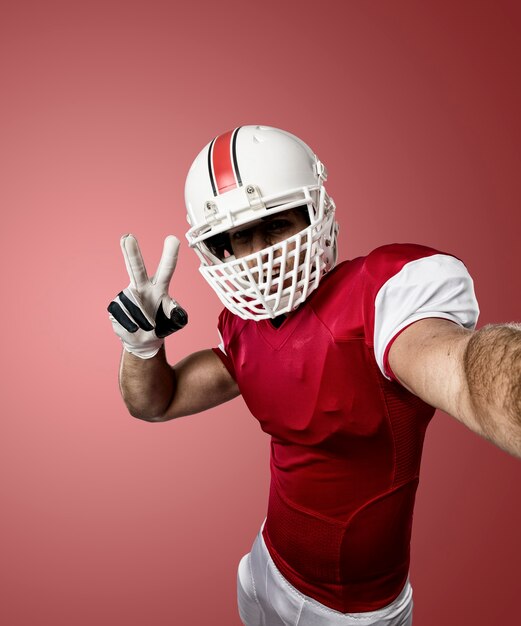 Giocatore di football con un'uniforme rossa che fa un selfie su una parete rossa