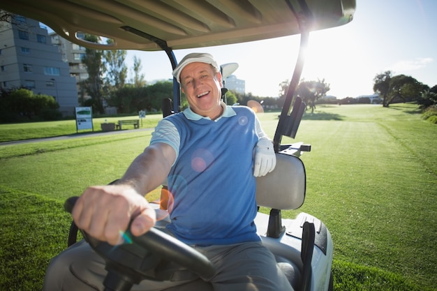 Giocatore di golf che guida il suo golf buggy e sorride alla macchina fotografica