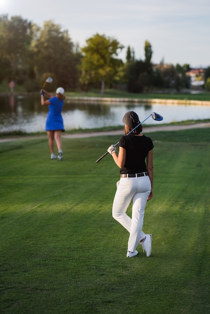 Giocatore di golf della donna che aspetta il suo turno per staccare dal tee-box. Vista da dietro della femmina che sta con il suo club di golf del driver il giorno soleggiato su un bello campo da golf.