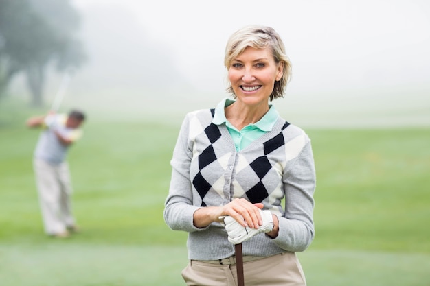Giocatore di golf della signora che sorride alla macchina fotografica con il partner dietro
