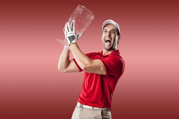 Giocatore di golf in una camicia rossa che celebra con un trofeo di vetro nelle sue mani, su uno sfondo rosso.