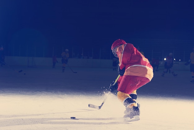 giocatore di hockey su ghiaccio dei bambini della ragazza teenager nell'azione che dà dei calci al disco con il bastone