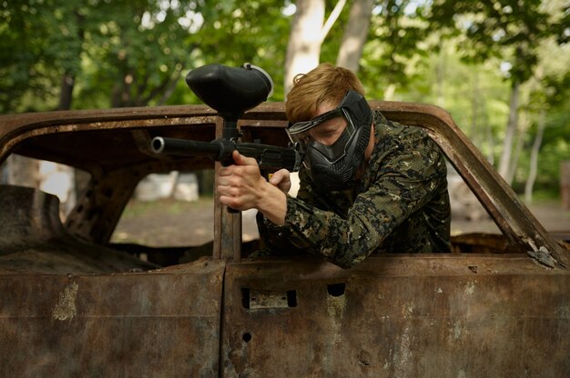 Giocatore di paintball in uniforme e maschera nella foresta