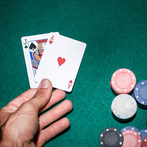 Giocatore di poker che tiene jack vanga e carta da gioco asso del cuore sul tavolo da poker