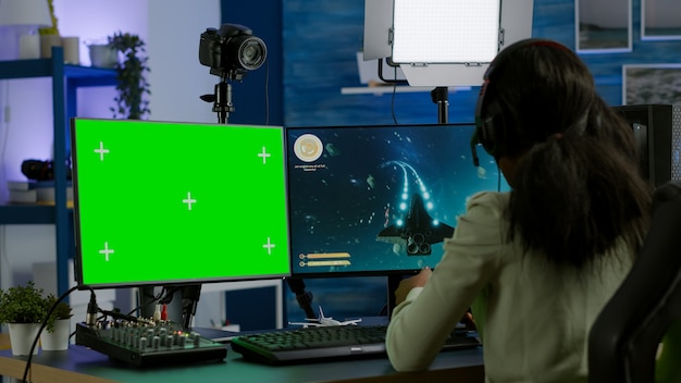 Giocatore di pro donna africana che gioca su un computer potente con schermo verde finto chroma key durante lo streaming della competizione online. Giocatore che utilizza un PC con giochi sparatutto in streaming desktop isolati con schermo verde