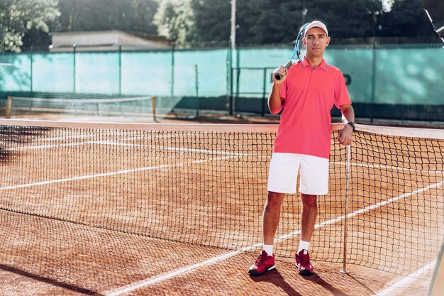 Giocatore di tennis dell'uomo di mezza età con la racchetta che sta sul campo vicino alla rete