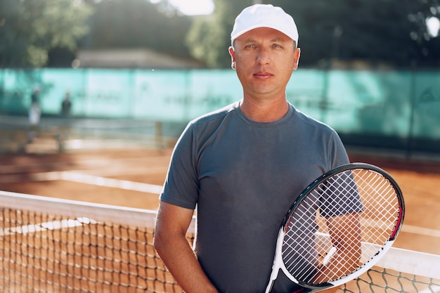 Giocatore di tennis dell'uomo di mezza età con la racchetta che sta sul campo vicino alla rete