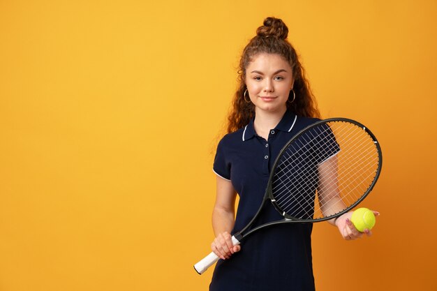 Giocatore di tennis della giovane donna che sta con la racchetta contro il fondo giallo