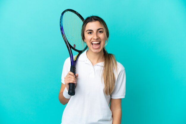 Giocatore di tennis della giovane donna isolato su fondo blu con l'espressione facciale di sorpresa