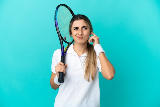 Giocatore di tennis della giovane donna isolato su fondo blu frustrato e che copre le orecchie