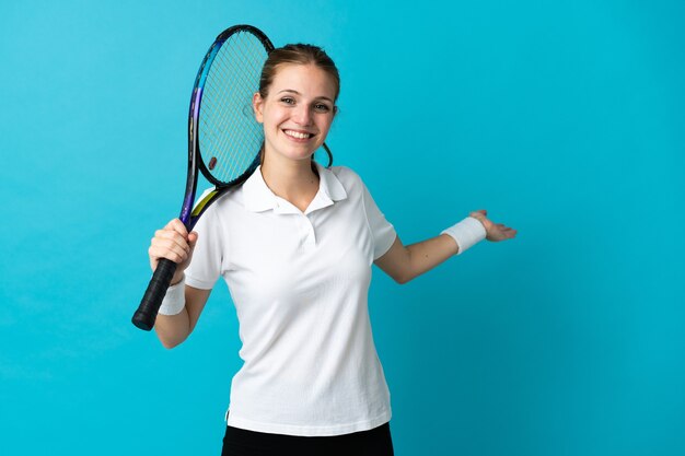 Giocatore di tennis della giovane donna isolato su priorità bassa blu che estende le mani a lato per invitare a venire