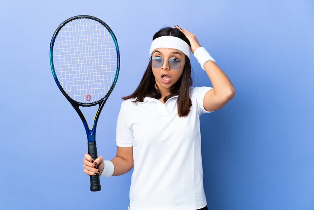 Giocatore di tennis della giovane donna sopra la parete isolata che fa gesto di sorpresa mentre guarda al lato