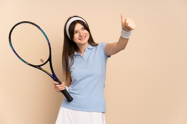 Giocatore di tennis della ragazza sopra la parete isolata che dà i pollici aumenta il gesto