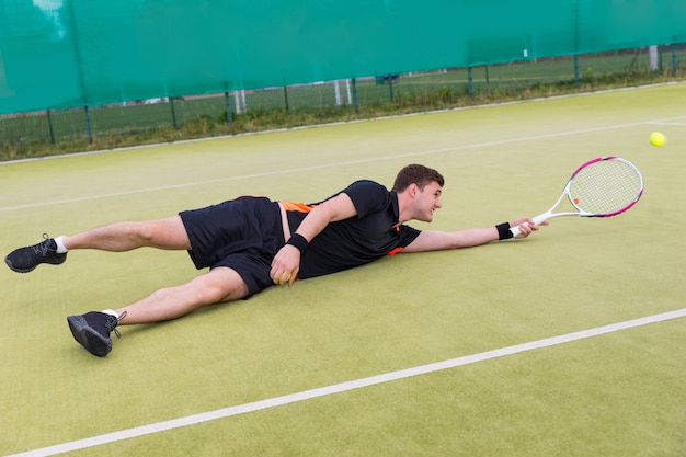 Giocatore di tennis maschio che indossa un abbigliamento sportivo in azione durante il gioco caduto su un campo