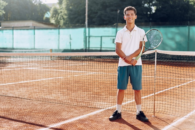 Giocatore di tennis uomo giovane razza mista con racchetta in piedi sul campo da tennis