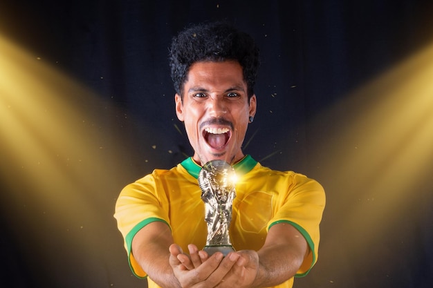 Giocatore nero di calcio brasiliano che tiene il trofeo del vincitore e festeggia