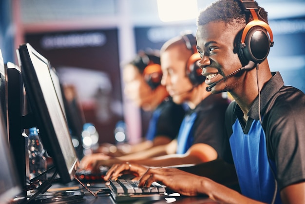 Giocatore professionista. Vista laterale di un giovane ragazzo africano eccitato, giocatore di cybersport maschio che indossa le cuffie che gioca ai videogiochi online mentre partecipa con la squadra al torneo di eSport