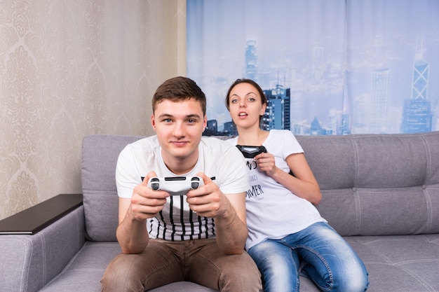 Giocatori maschi e femmine che giocano a videogiochi seduti insieme su un divano a casa in un'atmosfera rilassata