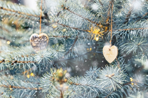 Giocattoli di legno naturali delle decorazioni rustiche di Natale a forma di cuore che appendono sull'albero di Natale fuori e che nevicano.