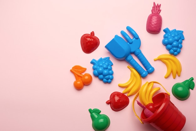 Giocattoli di plastica per bambini sotto forma di frutta e un secchio su uno sfondo rosa