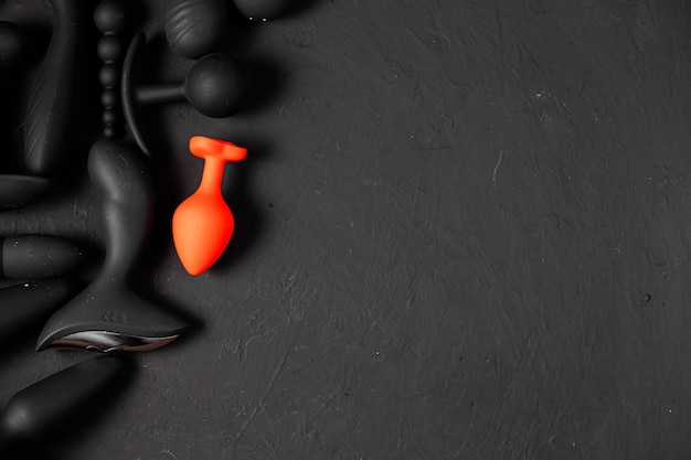 Giocattoli erotici per il piacere su sfondo nero Gadget sessuali e dispositivi per la masturbazione Dildo rosa circondato da giocattoli sessuali in gomma nera e silicone plug anali vibratori palle vaginali Vista dall'alto