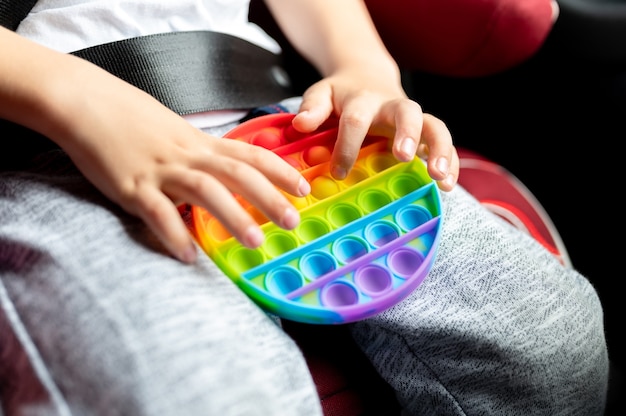 Giocattoli pop sensoriali antistress nelle mani di un bambino. un ragazzino felice gioca con un semplice giocattolo con fossette in macchina.