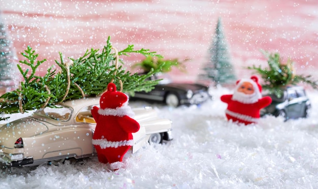 Giocattolo Babbo Natale nella foresta tra i cumuli di neve ondeggia verso le auto che consegnano alberi di Natale