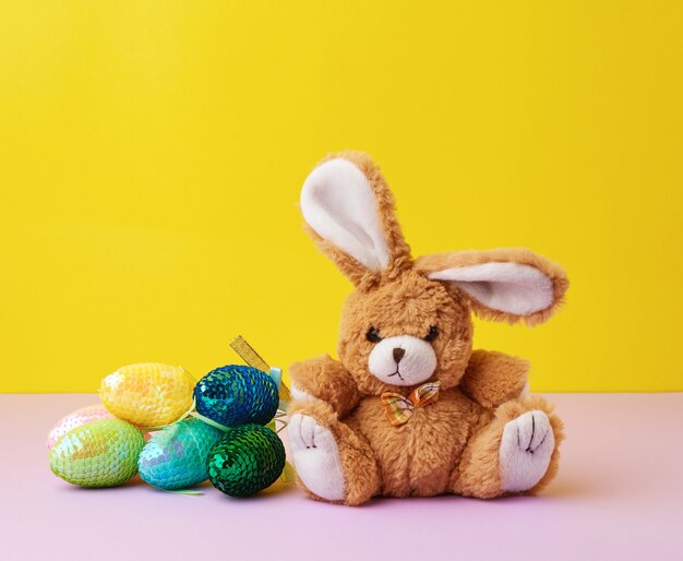 Giocattolo carino coniglio e uova di Pasqua decorative con paillettes su una superficie gialla