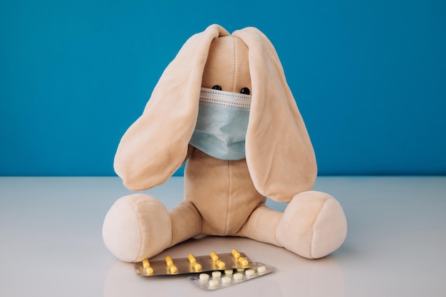 Giocattolo coniglietto in maschera con pillole su sfondo blu Concetto di malattie dei bambini