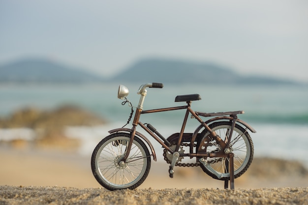 Giocattolo del trasporto di biciclette sulla spiaggia del mare della sabbia nel cielo di tramonto di sera