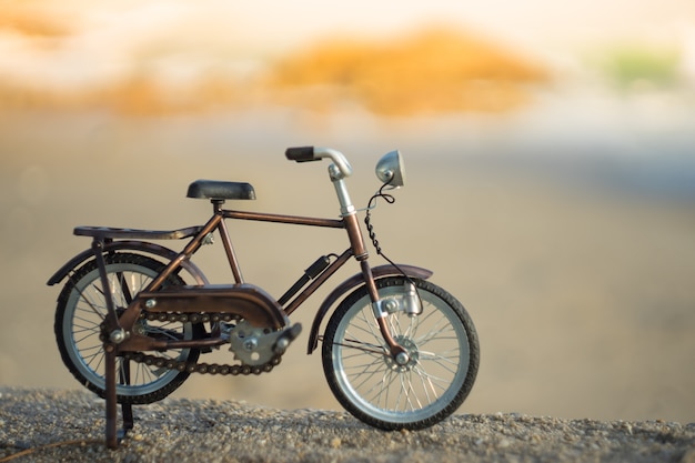 Giocattolo del trasporto di biciclette sulla spiaggia del mare della sabbia nel cielo di tramonto di sera