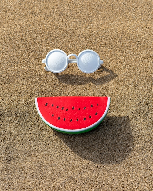 Giocattolo di anguria con occhiali da sole sulla sabbia