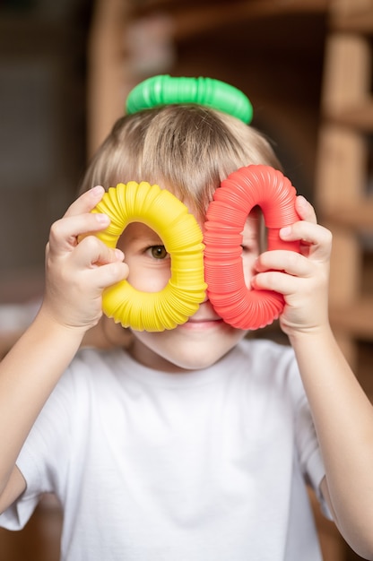 Giocattolo di plastica con tubo pop sensoriale anti stress nelle mani dei bambini. un piccolo bambino felice gioca con un giocattolo di fidget poptube a casa. bambini che tengono e giocano a tubi pop colori multicolori, tendenza 2021 anno