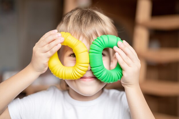 Giocattolo di plastica con tubo pop sensoriale anti stress nelle mani dei bambini. un piccolo bambino felice gioca con un giocattolo di fidget poptube a casa. bambini che tengono e giocano a tubo pop di colore giallo e verde, tendenza 2021 anno