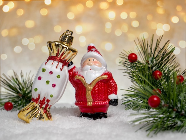 Giocattolo divertente Babbo Natale con la caramella su una superficie di neve invernale con bokeh colorato e rami di abete. Natale o concetto di inverno.