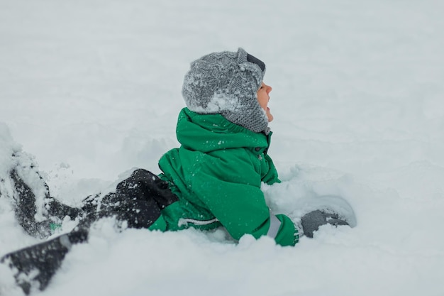 Giochi d'inverno all'aria apertaUn ragazzino in tuta verde gioca nella neve e scolpisce un pupazzo di neve