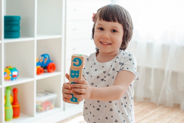 Giochi da bambini con blocchi di legno con lettere sul pavimento nella stanza una bambina sta costruendo una torre a casa o nella scuola materna.